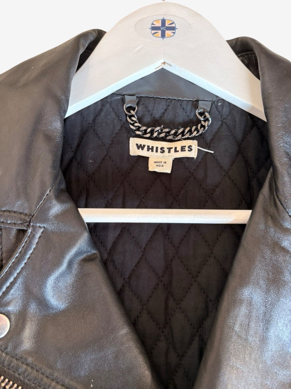 A close-up of a black leather jacket hanging on a white hanger. The interior shows a black quilted lining with a visible 'WHISTLES' brand label and a silver-tone chain detail.
