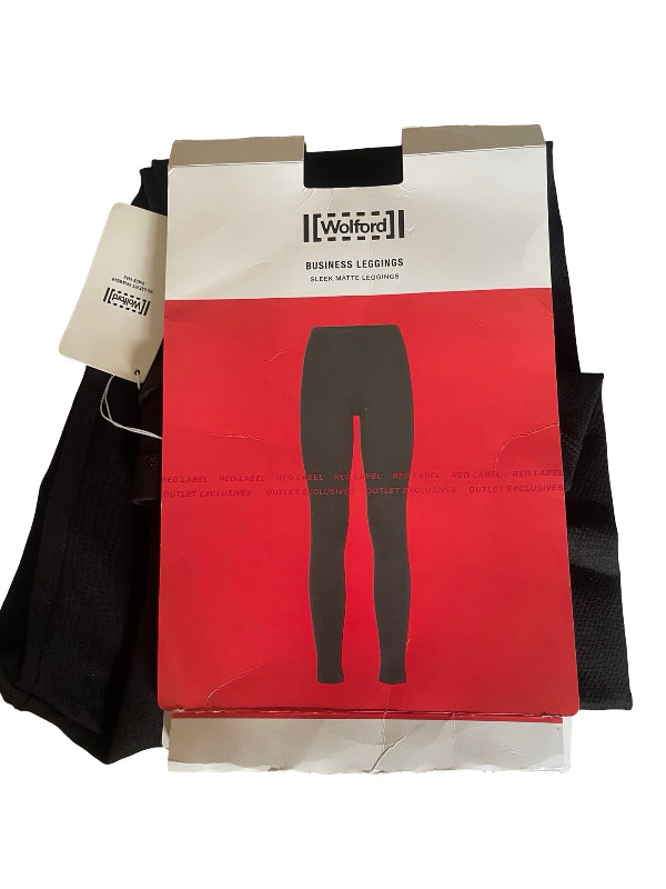 A pair of black leggings in retail packaging from the brand Wolford, featuring a red and white box with a black silhouette of the leggings and a hanging product tag.