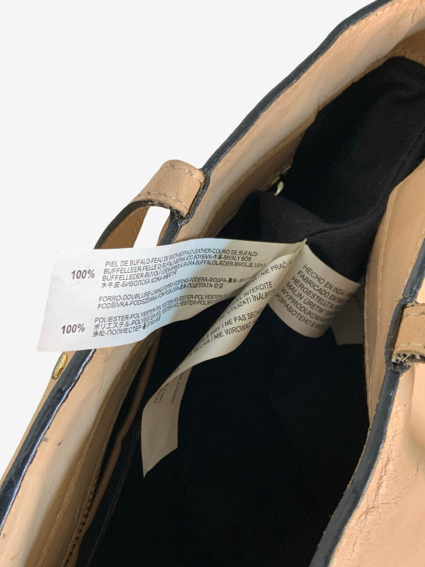 Close-up of a beige leather handbag interior showing a white care tag with printed text and a black fabric lining.
