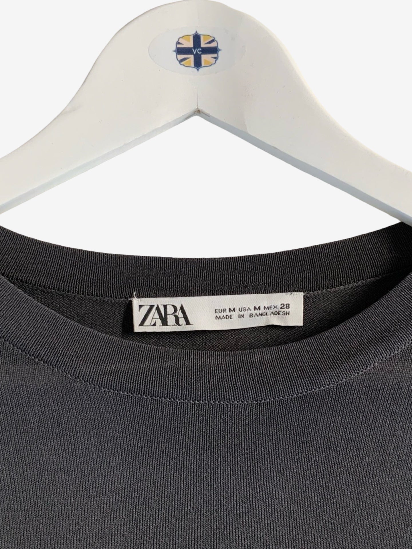 Close-up of a dark charcoal gray ribbed knit top hanging on a white hanger with a visible Zara neck label.